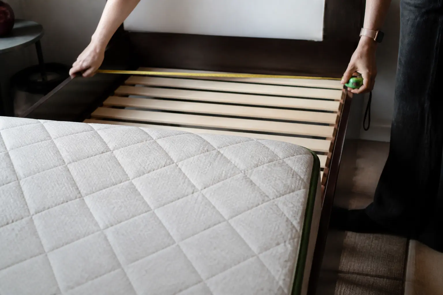 Mètre ruban mesurant la largeur d’un lit dans une chambre compacte, illustrant les dimensions lit.