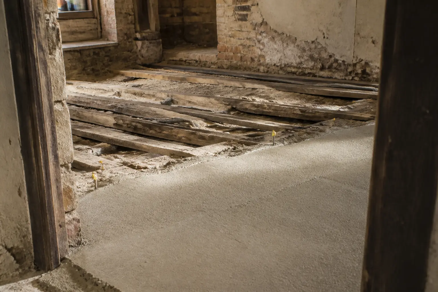 Chape allégée en pose sur vieux plancher bois, sol irrégulier, solives apparentes et lumière naturelle douce.