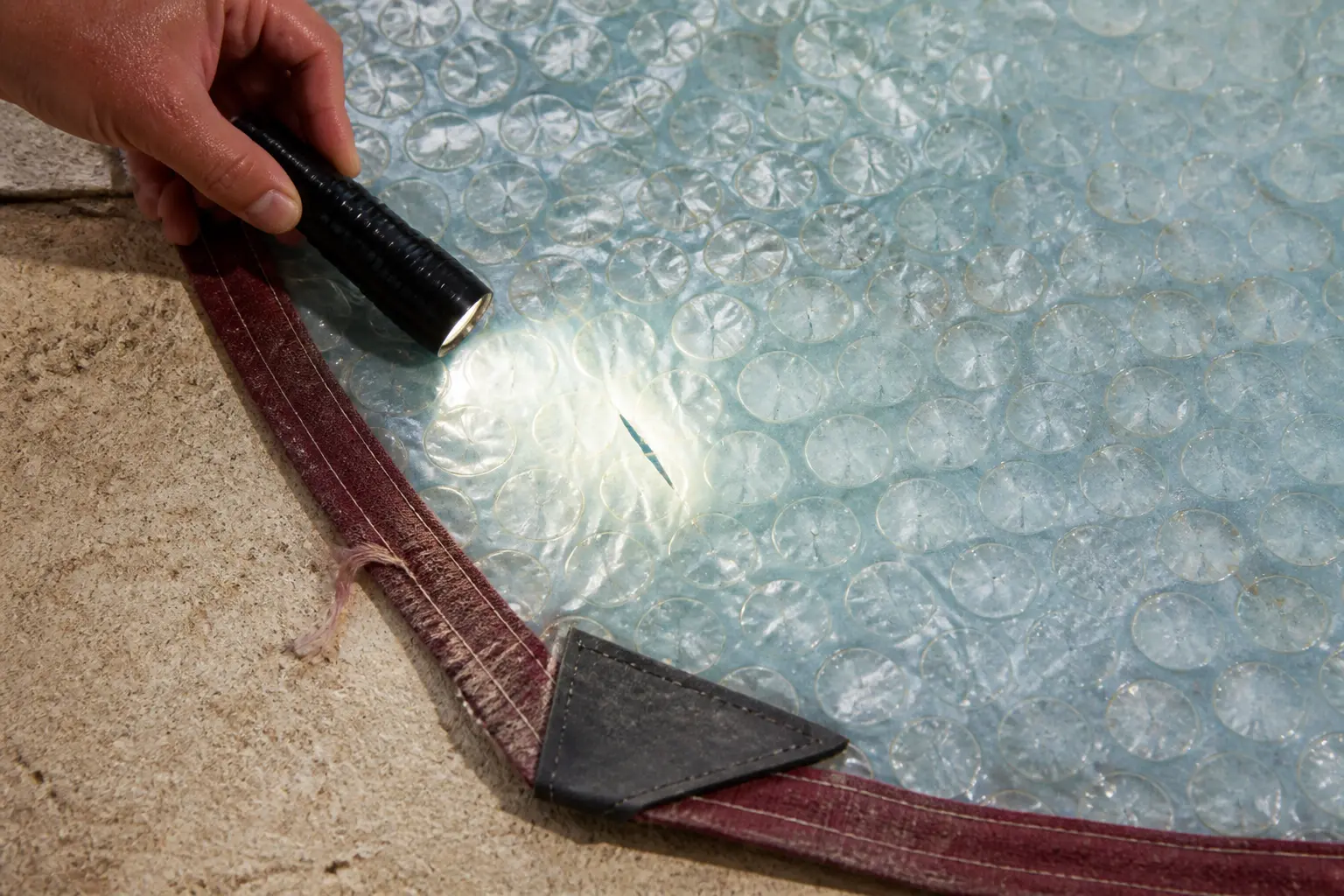 Comment coudre une bâche à bulle : gros plan d’une bâche de piscine avec petite déchirure, bord effiloché et angle renforcé inspectés