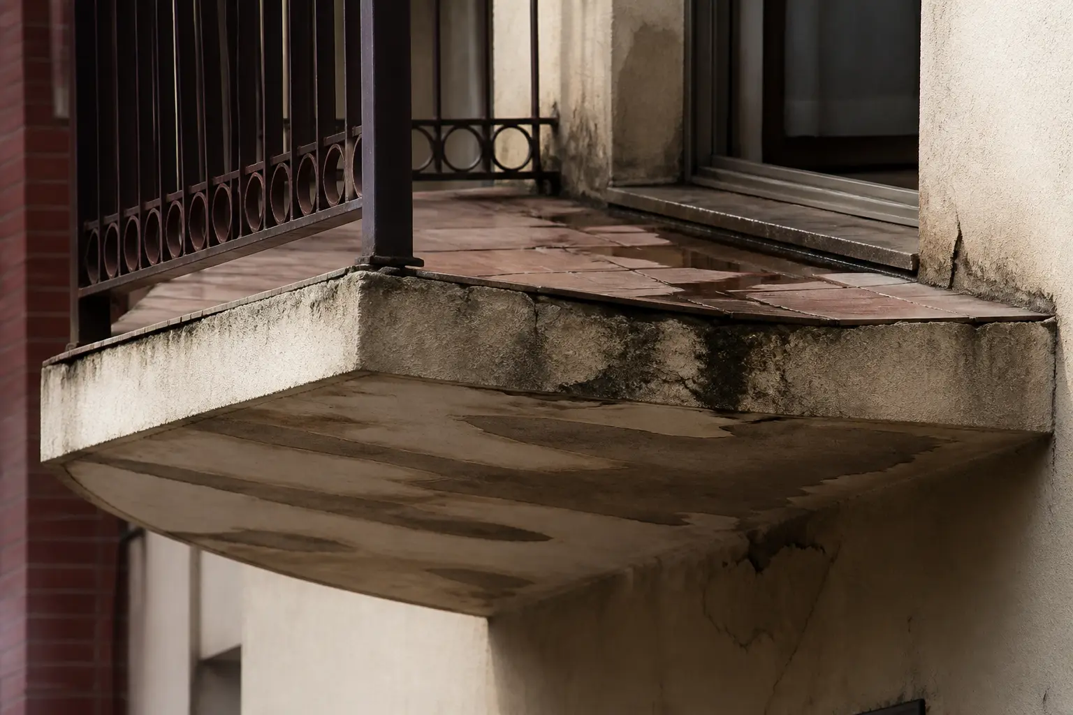 etancheite balcon : balcon d’immeuble avec fissures, joints abîmés et traces d’humidité sous la dalle, eau stagnante près du seuil